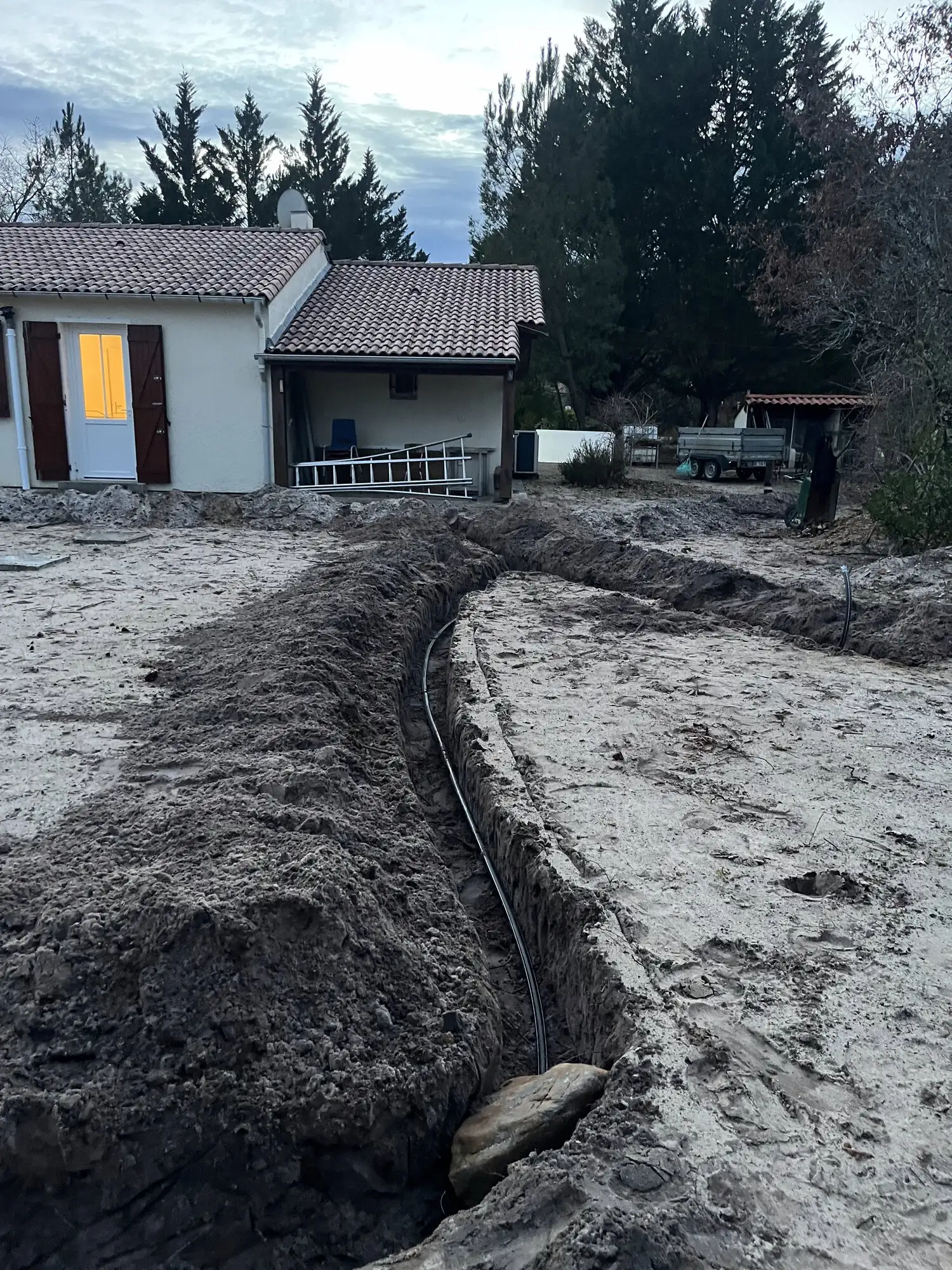Tranchée creusée dans le sable et tuyau d'arrosage automatique déroulé le long d'une maison