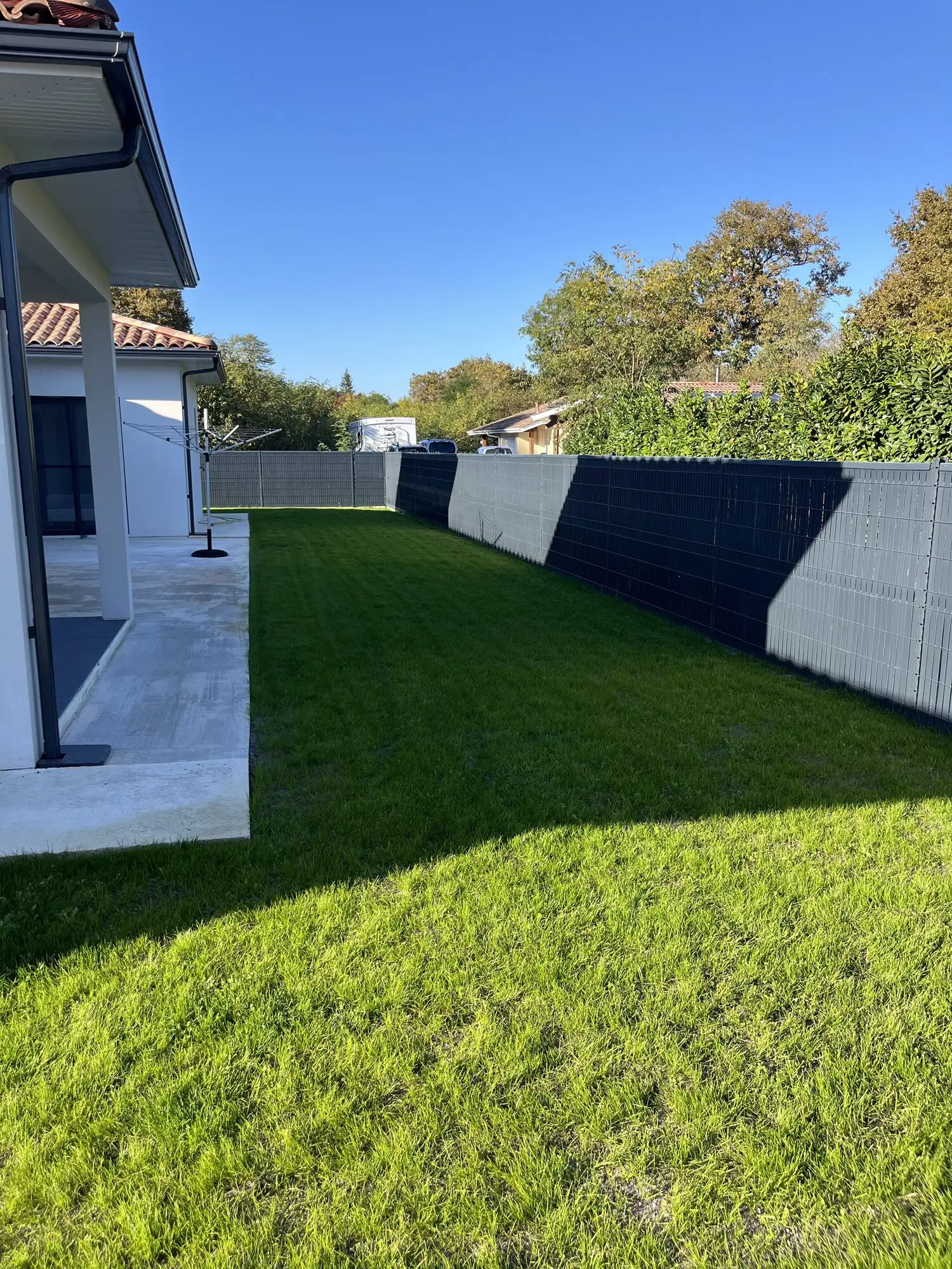 Pelouse installée devant la terrasse, bordures nettes le long de la clôture